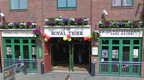 The pub sits on the high street and has green glass windows either side of the entrance.