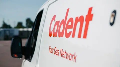 A white Cadent Gas transit van. The picture is taken of the side of the van with orange writing on the side which says Cadent, Your Gas Network, on it.