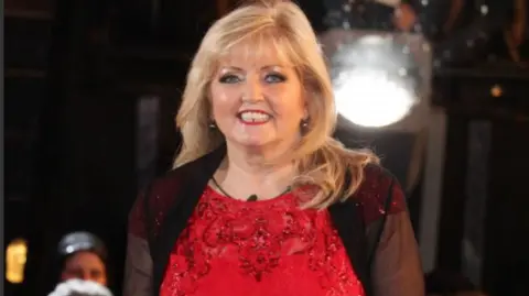 PA Media Linda Nolan, wearing a red dress, smiles as she leaves the Celebrity Big Brother house in 2014