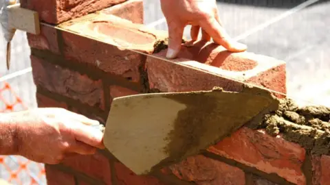 Bricklayer at work on house extension bricklaying a course of bricks building site