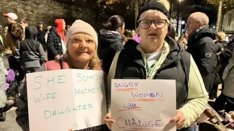 Liz Campbell and Collette McCallion stand holing signs at a rally in Derry

