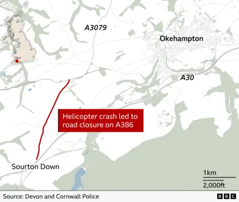 A simplified map of part of Devon in south‑west England shows the area around Okehampton and Sourton Down. The town of Okehampton is labelled on the right, with major roads including the A30 running east–west and the A3079 north of the town. A section of the A386 southwest of Okehampton is highlighted in red, indicating a closure. The highlighted stretch runs roughly north–south near Sourton Down. A red text box on the map reads: “Helicopter crash led to road closure on A386.” In the lower left corner is a small inset map of the United Kingdom with a red dot marking the location in the southwest of England. A scale bar in the lower right shows distances of 1 km and 2,000 ft. At the bottom, the source is credited as “Devon and Cornwall Police,” alongside BBC branding.