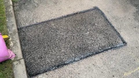 Chris McHugh/BBC A top down image of a completed, filled pothole. The square area is a fresh black colour with new tarmac, with a black border around the outside. The old grey tarmac can be seen surrounding it. 