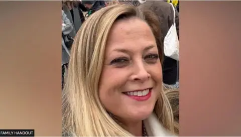 Annabel Rook is looking at the camera smiling. She has long blonde hair and is wearing make up. There are people in the background behind her and the photo was taken outside.