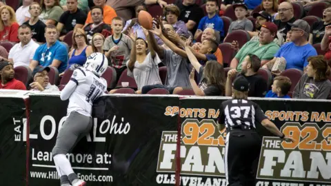 Getty Images Fans reach for a football after it deflects into the stands during an indoor arena league American Football match