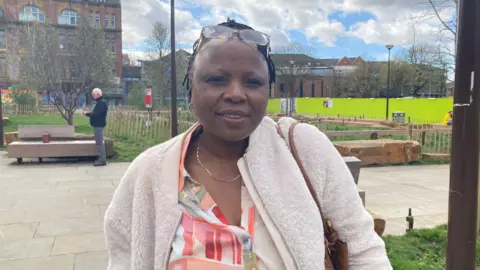 A woman wearing a sheepskin jacket and a beige and red blouse with black hair and glasses on her head