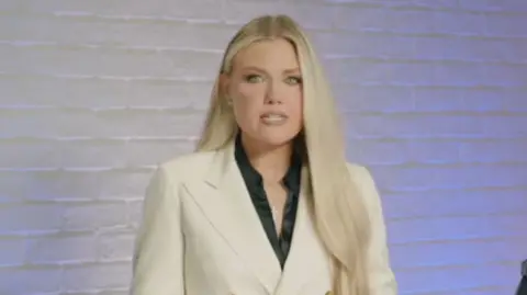 Turning Point USA Erica Kirk Captura de tela. Ela tem longos cabelos loiros e vestindo um blazer branco com uma camisa preta no fundo.