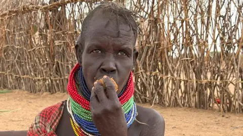 A woman with beaded, colourful necklaces around her neck is putting some food in her mouth.