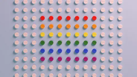 Getty Images Collums of white pills sit on a blue backround. There are 10 rows, with 13 pills in each row. In the centre of these pills there are muti-coloured ones. Each row is a different colour, from top to bottom they're red, orange, yellow, green, blue and purple.