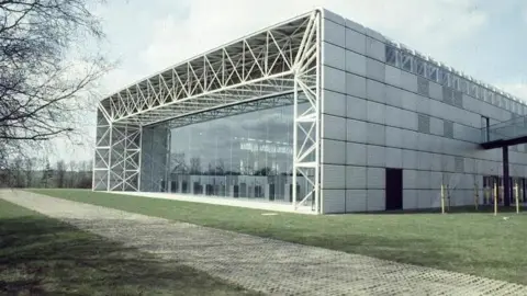 A big grey and white building fills up most of the picture. The front of the Sainsbury Centre is seen, with a massive glass window filling up the whole of the front of the building. 