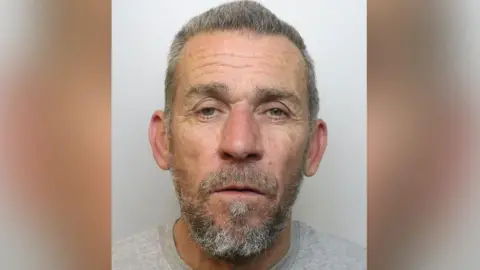 Mugshot of Gary Selwood. He has grey hair and a beard and is wearing a grey shirt.