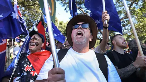 Getty Images Anti-immigration protesters hold flags and chant during speeches at Victoria Park on August 31, 2025 in Sydney, Australia.