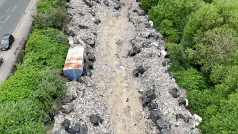 Mounds of rubbish piled up with trees surrounding both sides