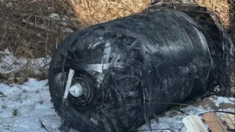 Adam Boruki, a cylindrical cylindrical tank measuring 1 meter at a distance of 1 meter on the icy ground next to a wire fence on the property of Adam Boruki. 