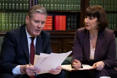 Getty Images Keir Starmer y Rachel Reeves están sentados en una oficina parlamentaria frente a libros encuadernados en cuero revisando archivos mientras se preparan para el presupuesto conservador de primavera en el Parlamento.