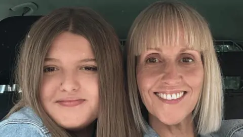 A mother and daughter pose for a selfie inside a car
