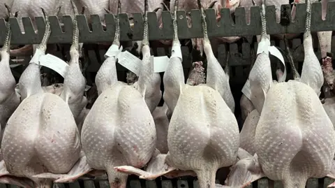 Shaun Whitmore/BBC Processed turkeys hang on hooks within a warehouse.