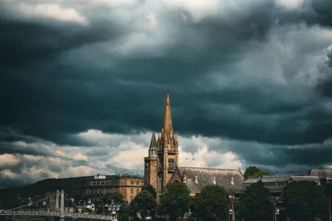 Ishan Acharya A dark, brooding cloudy sky over a city centre, with a church steeple in the middle