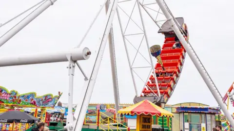 A side view of a pirate ship as it swings into the sky, with people on board, on the fairground attraction.