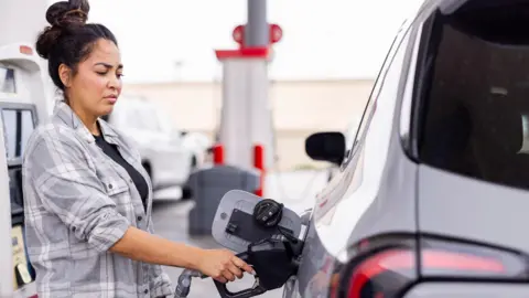 Woman wearing a grey shirt fills up her car at a gas station