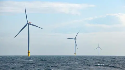 Three offshore wind turbines in the North Sea. Blue sky with clouds