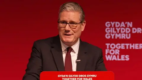 Sir Keir stood at a lecturn at Welsh Labour conference, with Together for Wales written in England and Welsh behind and in front of him. He is wearing a black suite, red tie and white shirt.