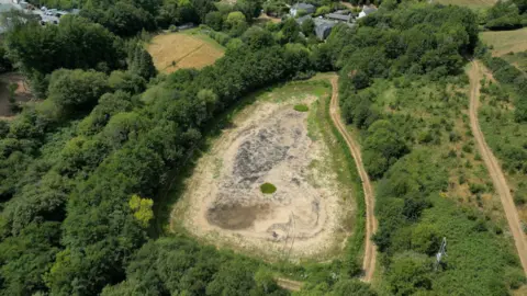 An overhead view of a reservoir in the countryside in Buckfastleigh which has no water in it.
