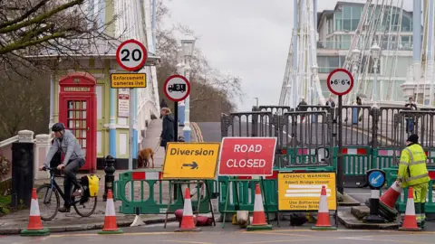Closure signage at the entrance of the bridge with fencing in place. A number of pedestrians and cyclists can be seen in the bridge but it is closed to traffic. 