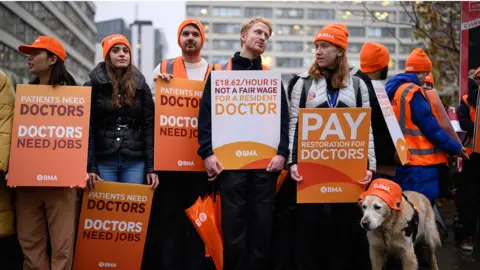 Getty Images Resident doctors wearing orange beanie hats and carrying orange placards bearing the wears Doctor Need Jobs