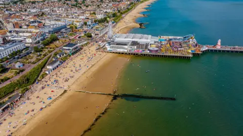 Getty Images An aerial shot of Clacton-on-Sea, Essex. A large beach lines the coast, with a pier covered in theme park rides stretching out to sea.