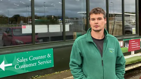 Matthew Brook is standing outside Brookridge Timber. He is wearing a green fleece and is looking at the camera.