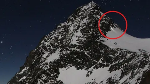 www.foto-webcam.eu A mountain peak with a red circle highlighting the man climbing down