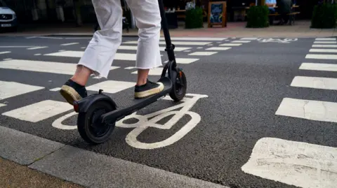 An e-scooter is moving on a cycle lane crossing in a town centre