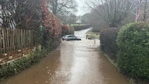 SCAS Flooded roads with grey car in the distance trapped by the flood.