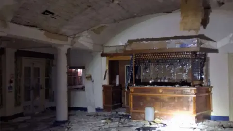 The interior of a club house with the ceiling haven fallen down and a bar covered in debris.
