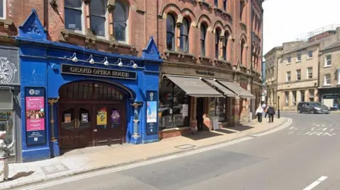 The Grand Opera House in York, a theatre in a curved red brick building. It has a blue painted front and a black and gold sign which sais 'grand opera house'
