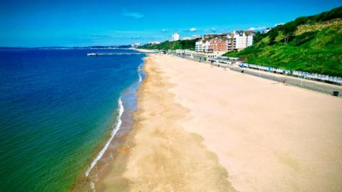 Boscombe pier can be seen in the distance but the photo is dominated by the clear yellow sand of Southbourne beach and the greenish blue colours of the sea