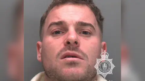 North Wales Police A mugshot of Dean Mears who has brown hair and stubble and is looking directly at the camera with a confused expression.