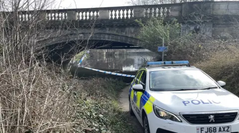 BBC A police cordon in place under St Mary's bridge, in Derby, with a police car nearby