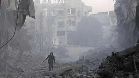 AFP A man walks through the rubble of buildings destroyed by Israeli airstrikes in Bureij refugee camp, central Gaza (12 January 2025)