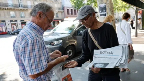 Reuters Ali Akbar, in a gray flat cap and black clothes, selling a copy of Le Monde to an old man in the streets of Paris