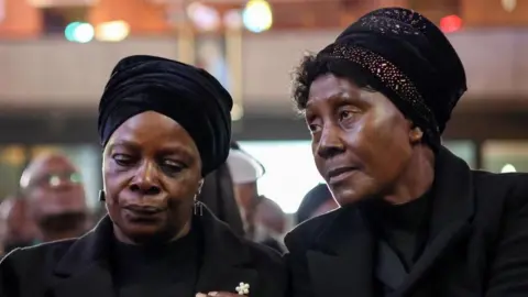 Reuters Esther Lungu, the widow of Zambia’s former president Edgar Lungu, is consoled by family memebrs during a service, after the Pretoria High Court halted the planned burial of the former president hours before the ceremony, following a weeks-long feud between Lungu's family and the Zambian government