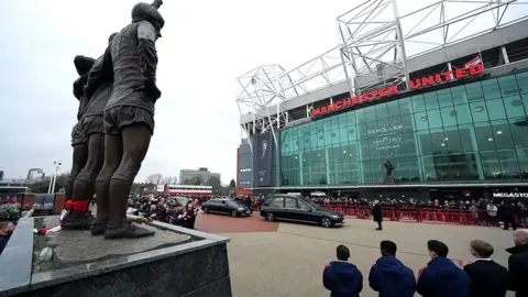 Thousands of fans clapping at Manchester United's Old Trafford as Denis Law's funeral cortege arrives