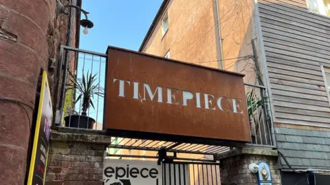 BBC An oxidised metal sign which says Timepiece above the entrance to the nightclub.