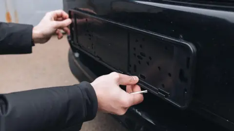 Getty Images Man unscrews license frame on car