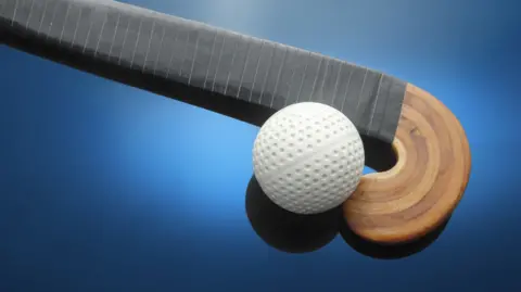 Close-up of white hockey ball and wooden stick on blue background