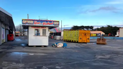 A derelict scene of an old unused token stand in an abandoned parking lot.