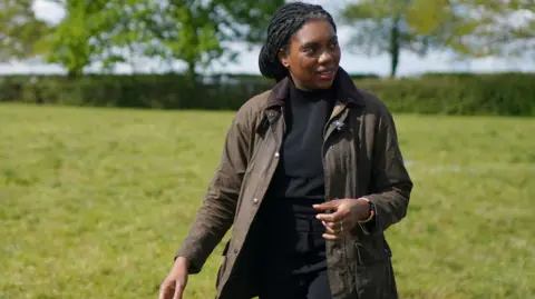 Kemi Badenoch dressed in a barbour coat standing in a field 
