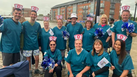 Two rows of people in nurses outfits are standing and kneeling, looking at the camera and smiling.