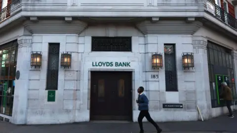 Getty Images Current image of bank in colour as a man wearing a short coat walks past